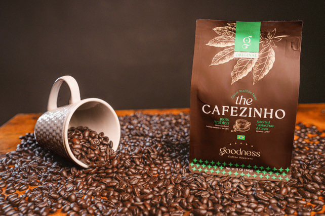 Embalagem do The Cafezinho ao lado de uma xícara, sobre grãos de café